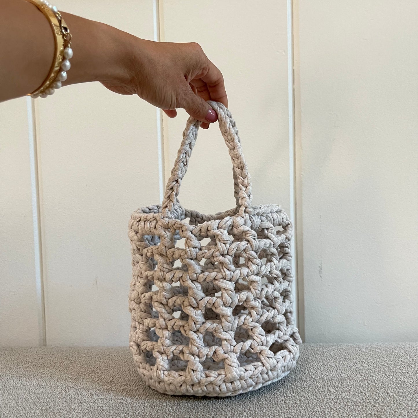 a hand holding a grey crocheted handbag. 
