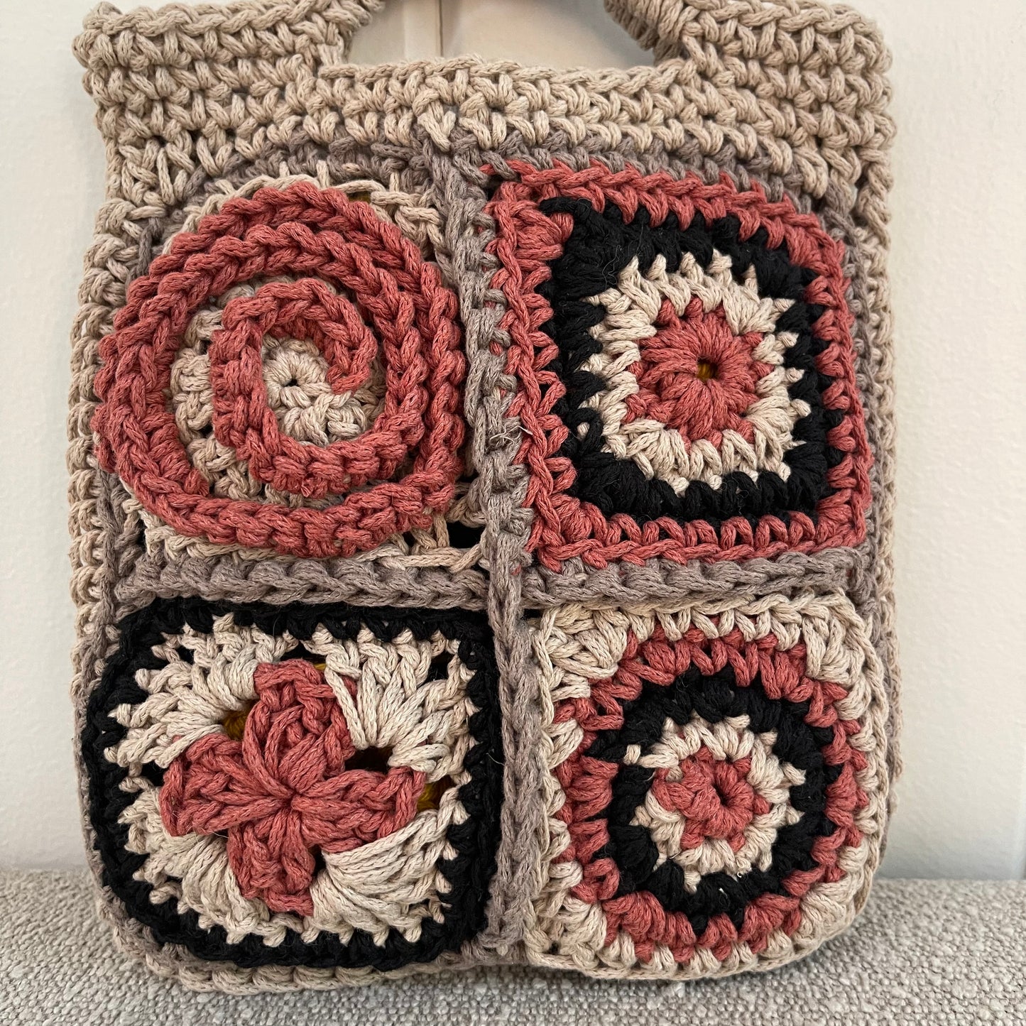 Close up photo of a crocheted granny square handbag in tan, grey, black and brick red. 