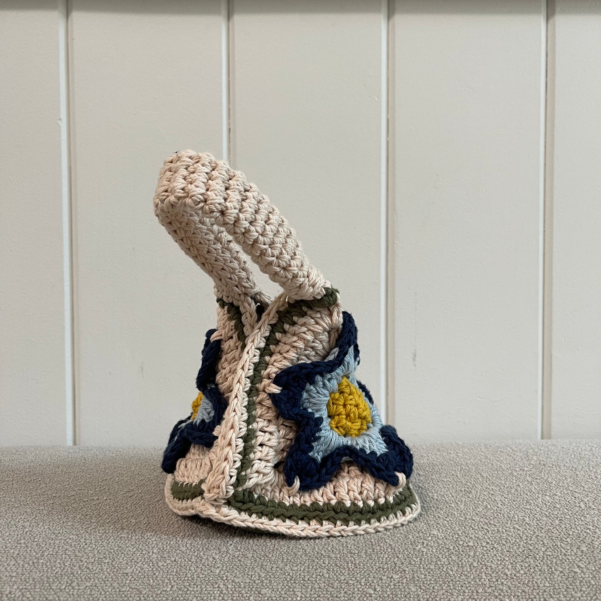 A crocheted handbag in cream, yellow, baby blue and navy blue. 