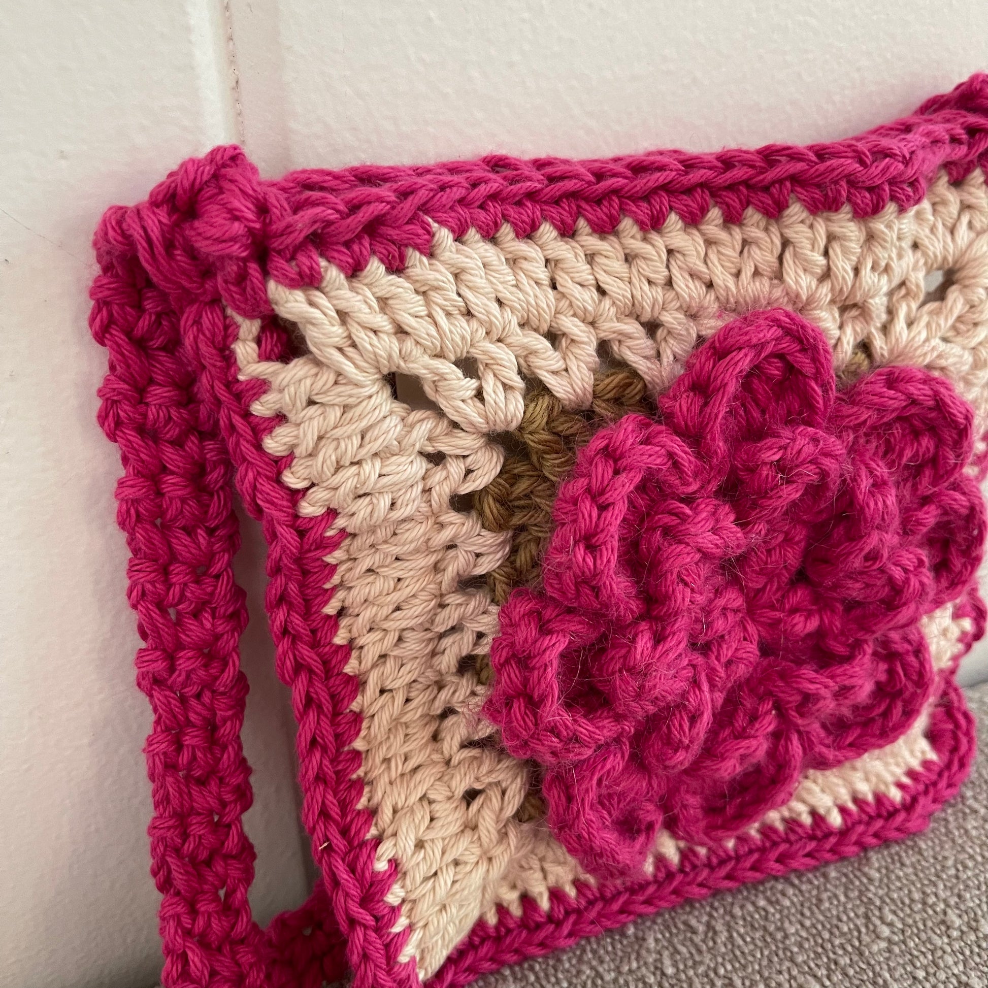Close up of a crocheted crossbody bag in pink and white. 