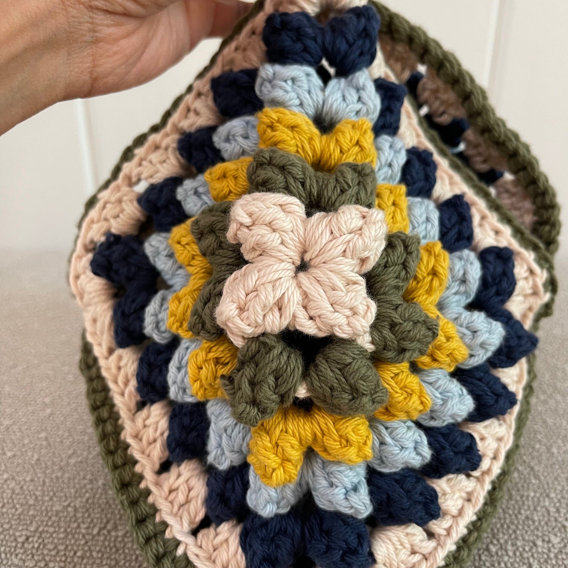 Close up of a crocheted handbag in cream, green, yellow, baby blue and navy blue. 