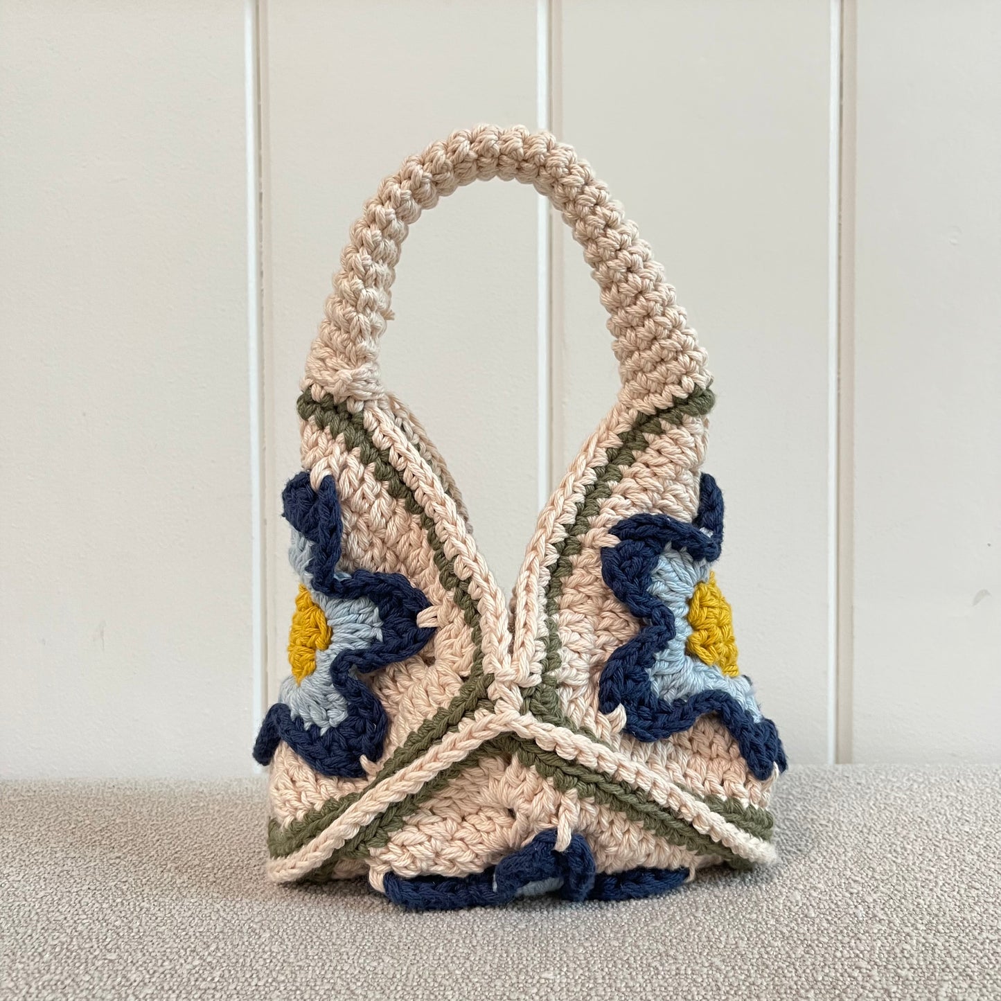 A crocheted handbag in cream, yellow, baby blue and navy blue. 