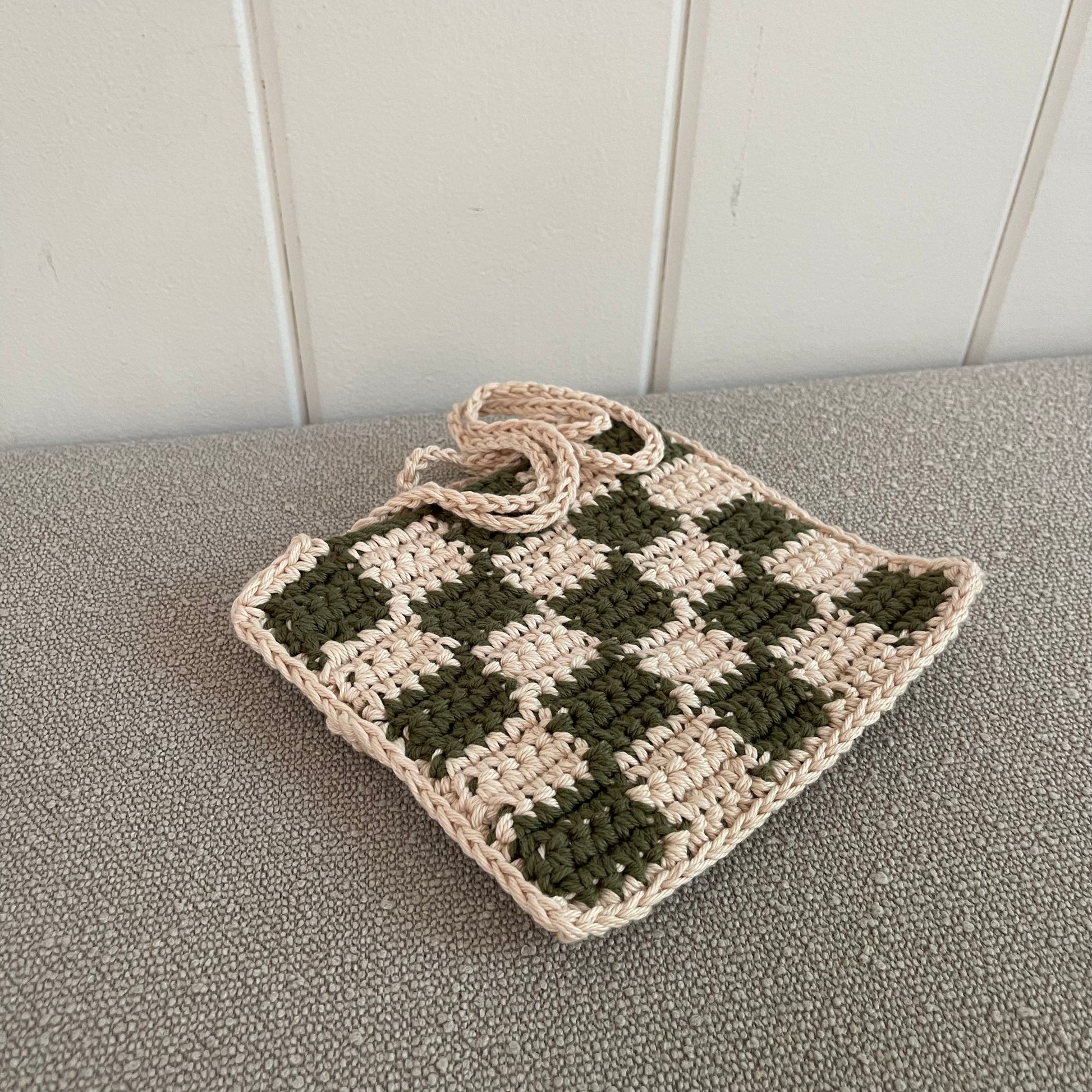 A closeup of a checkered crochet shoulder bag in green and cream. 