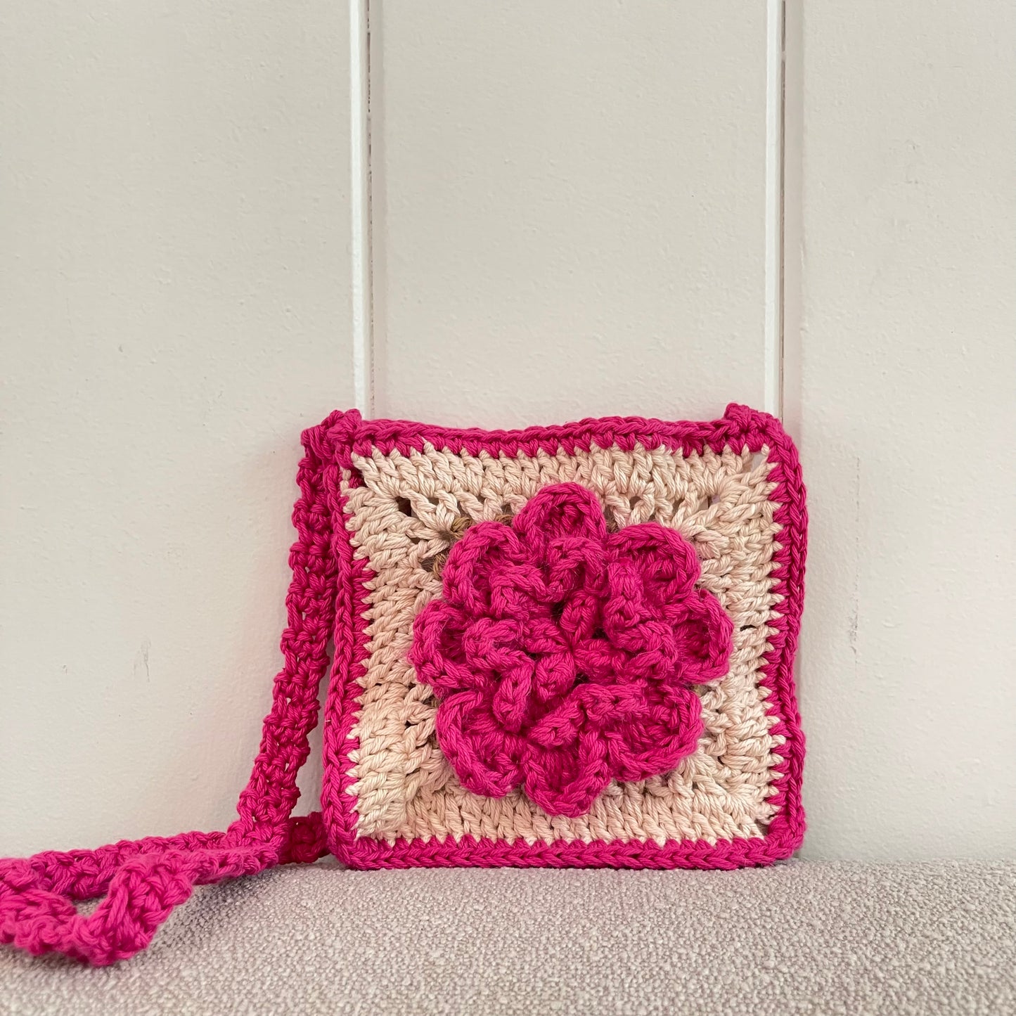 Crocheted granny square crossbody bag with a rose. The bag is pink and white. 