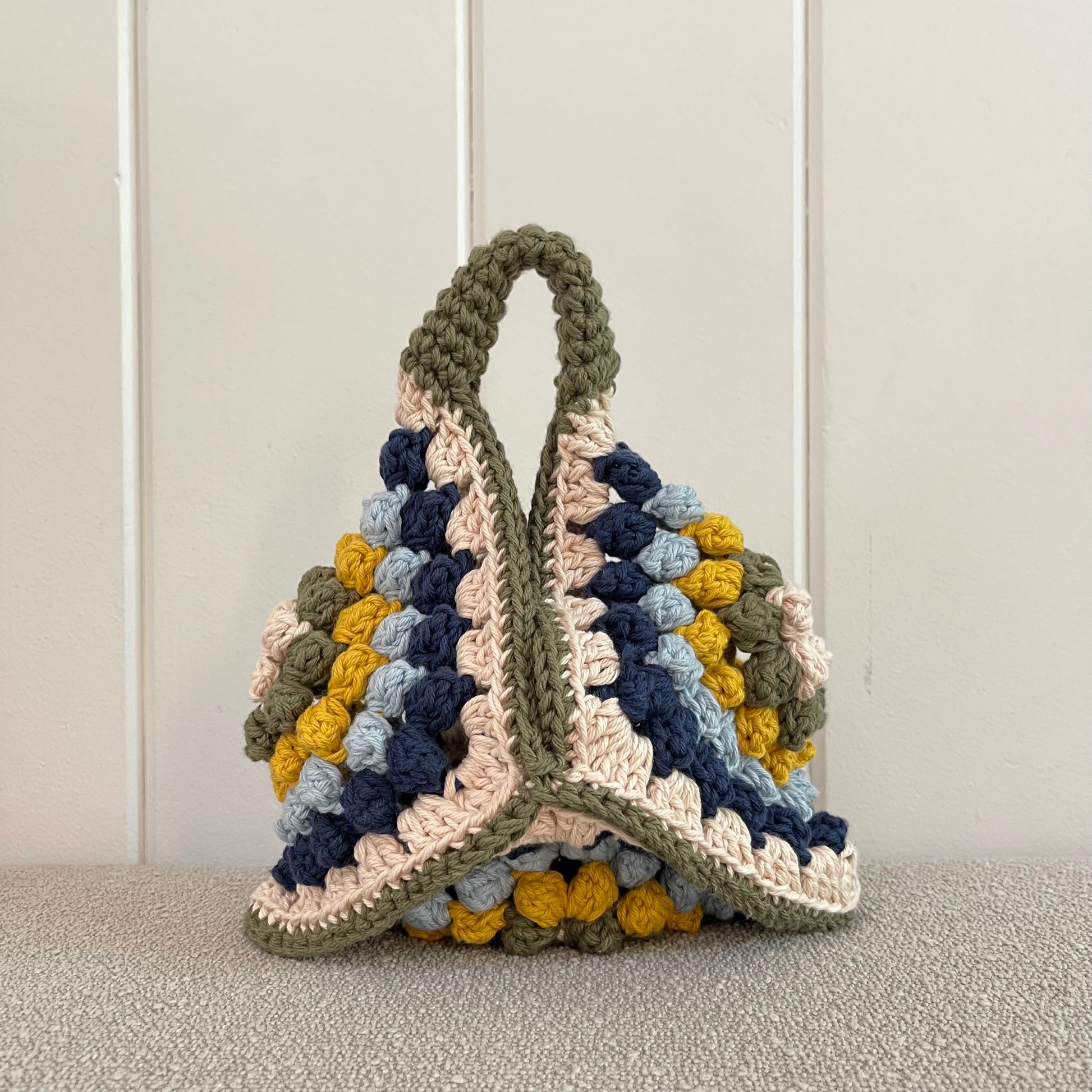 a crocheted handbag in cream, green, yellow, baby blue and navy blue. 
