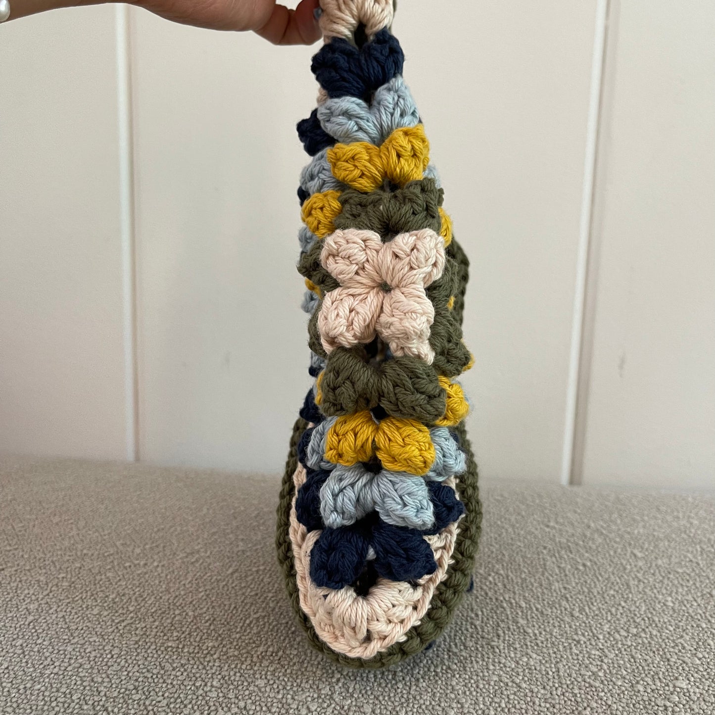 Sideview of a crocheted handbag in cream, green, yellow, baby blue and navy blue. 