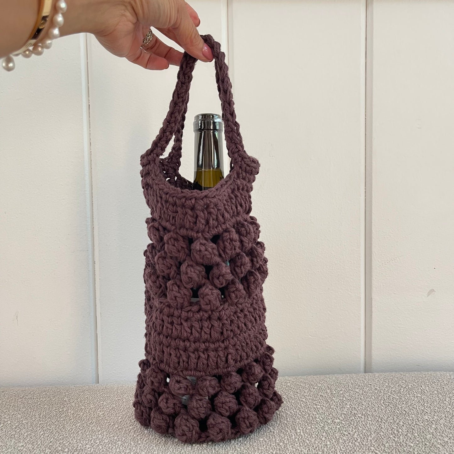 Photo of a hand holding a brown crochet wine bag. 