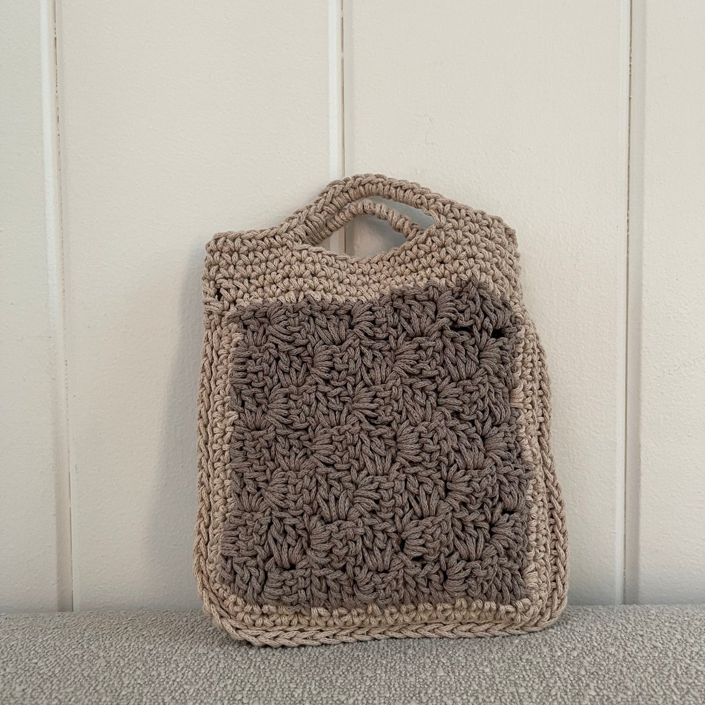 The backside of a crocheted granny square handbag in tan and grey. 