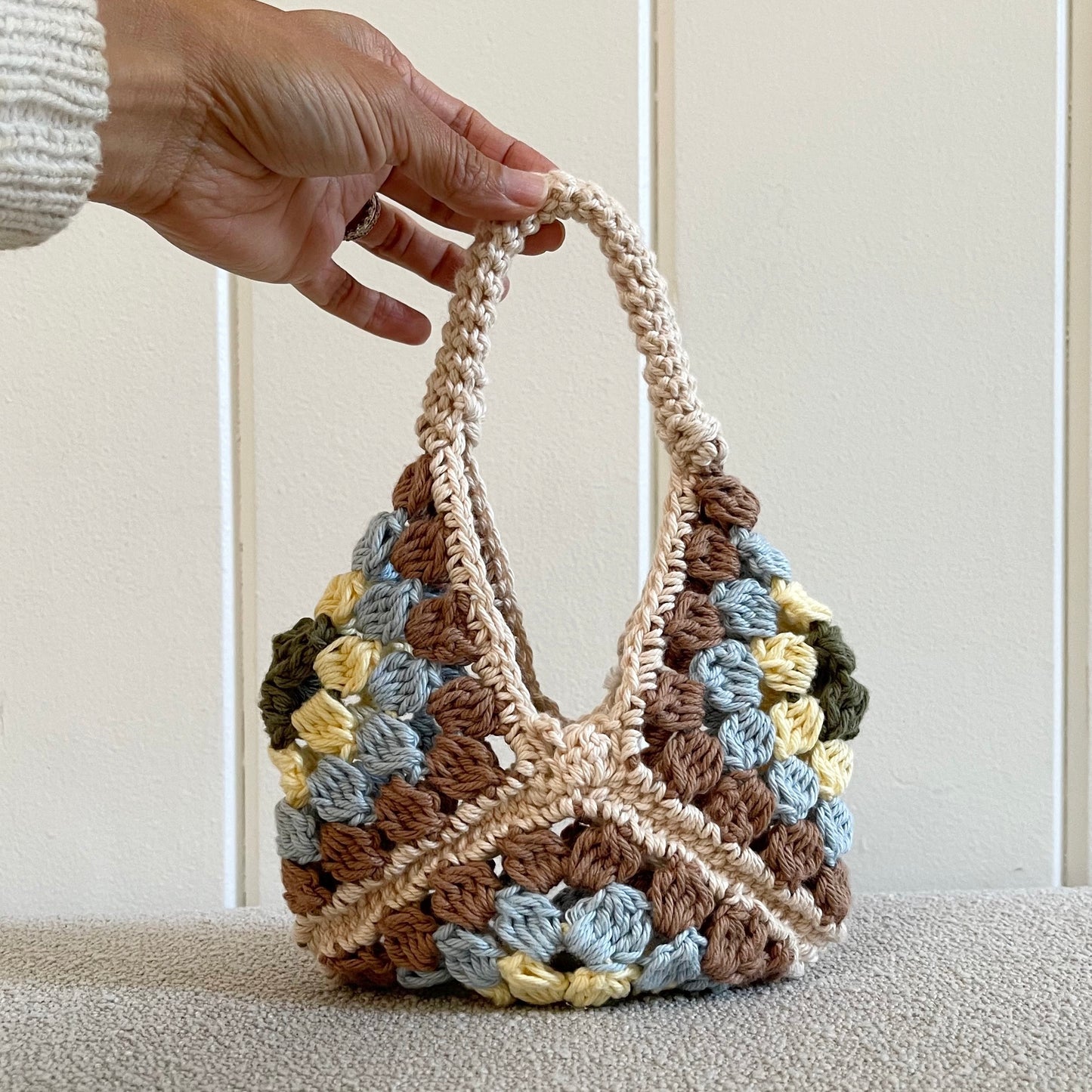 A mini crochet granny square handbag  Measures 7 by 7 inches + the hand strap. It is great for a cell phone, keys and some touch up makeup. Perfect for a night out.  Made of 100% cotton in colors cream, light brown, baby blue, light yellow and military green. 