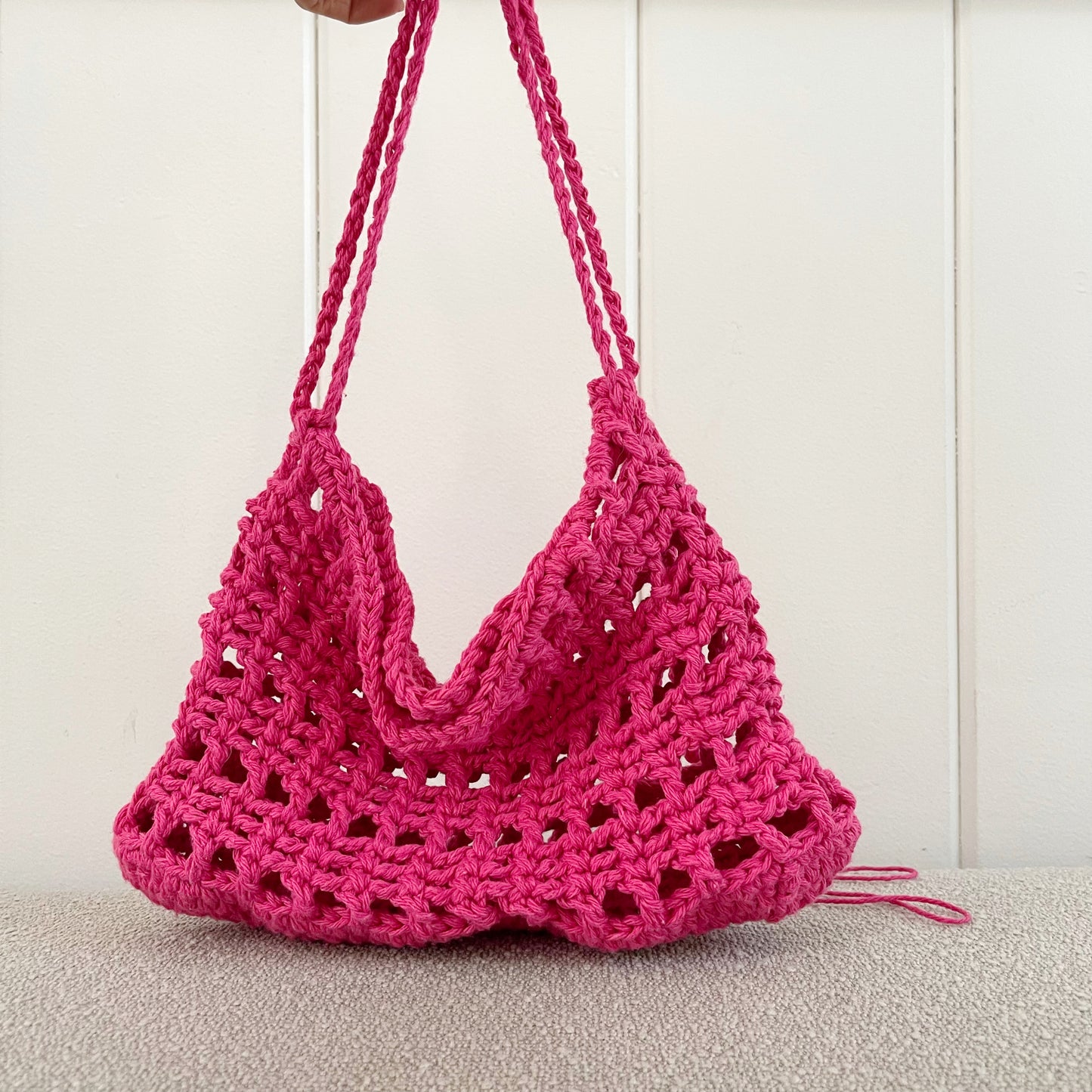 A picture of a crochet mesh handbag in hot pink  Measures 11" wide x 8" tall + a shoulder strap. Made of 100% cotton.   