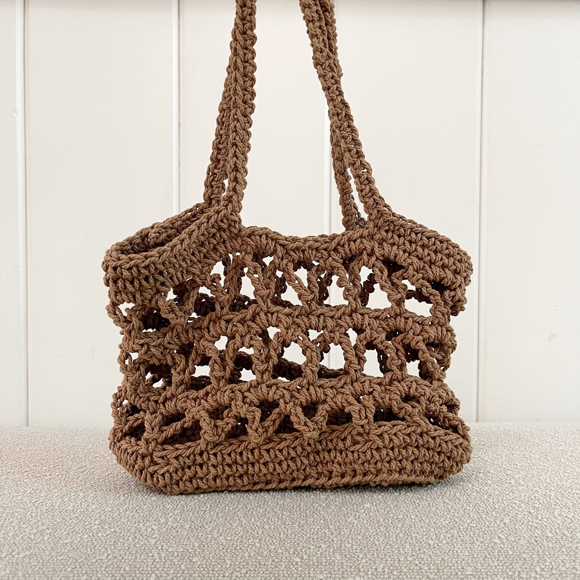 Picture of a crochet mesh handbag in brown. A great addition to any neutral wardrobe.   Measures 10" wide x 9" tall + a shoulder strap. Made of 100% cotton in brown. 