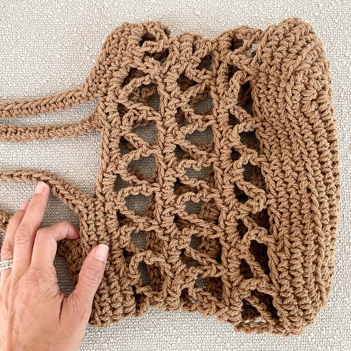 Picture of a crochet mesh handbag in brown with a closeup of the mesh design. A great addition to any neutral wardrobe. Measures 10" wide x 9" tall + a shoulder strap. Made of 100% cotton in brown.