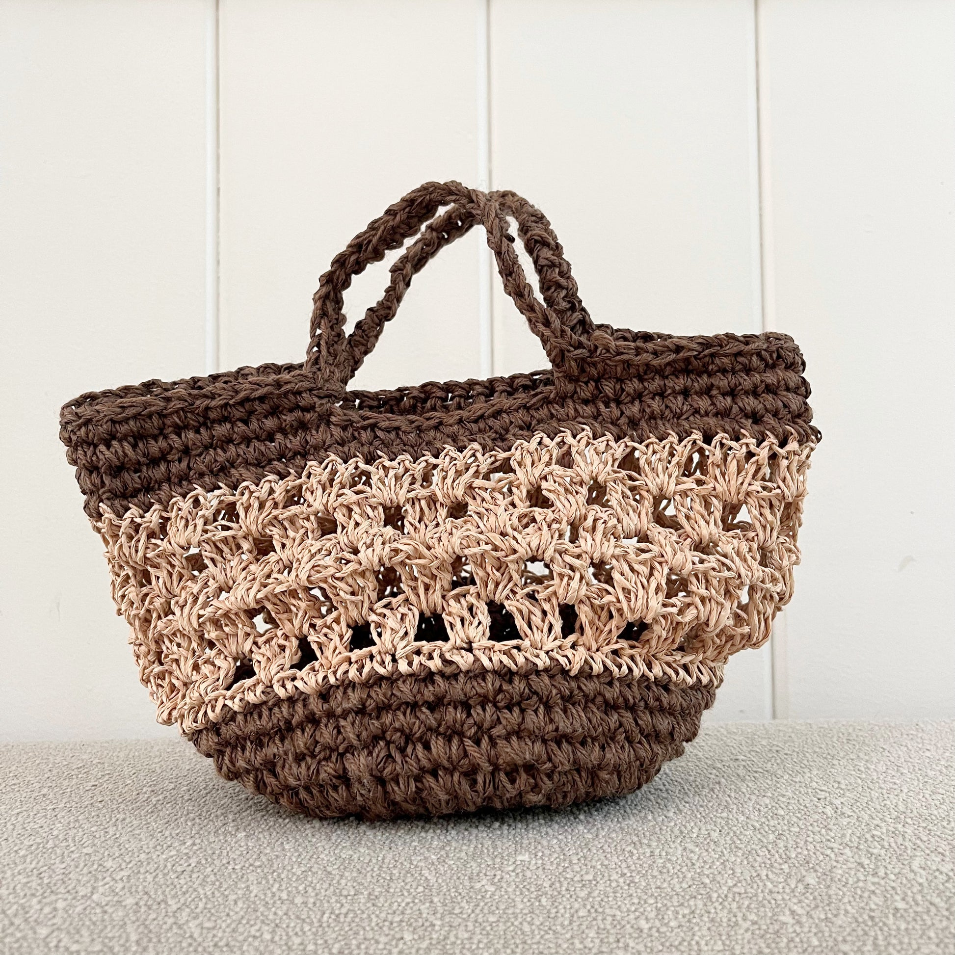 A picture of a Crochet handbag. A great addition to any neutral wardrobe.   Measures 12" wide x 8" tall + a hand strap. Made of raffia and cotton yarn. The top has hidden wire, to help keep it open when needed  